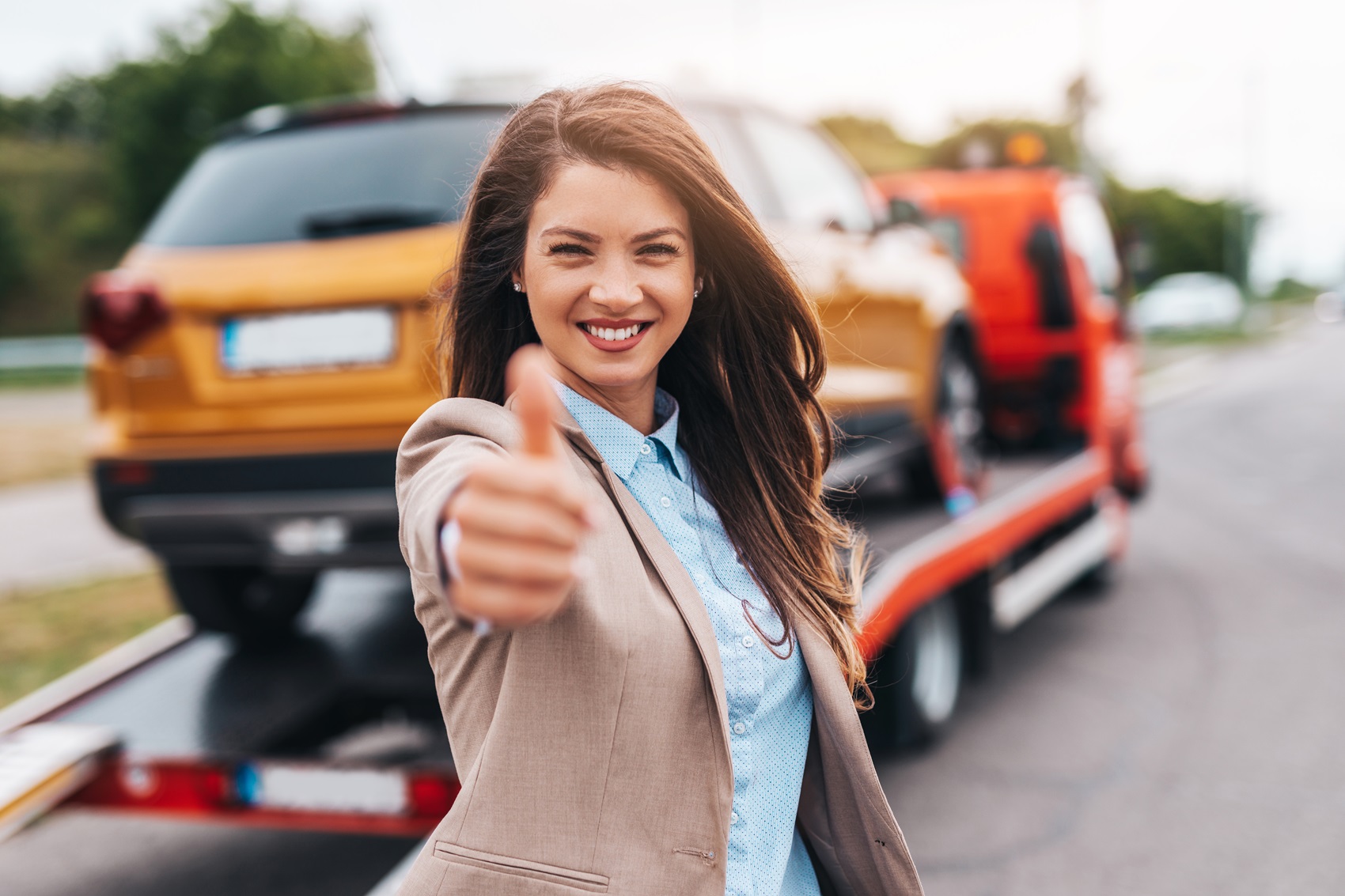 woman putting a thumbs up with car on tow truck in background